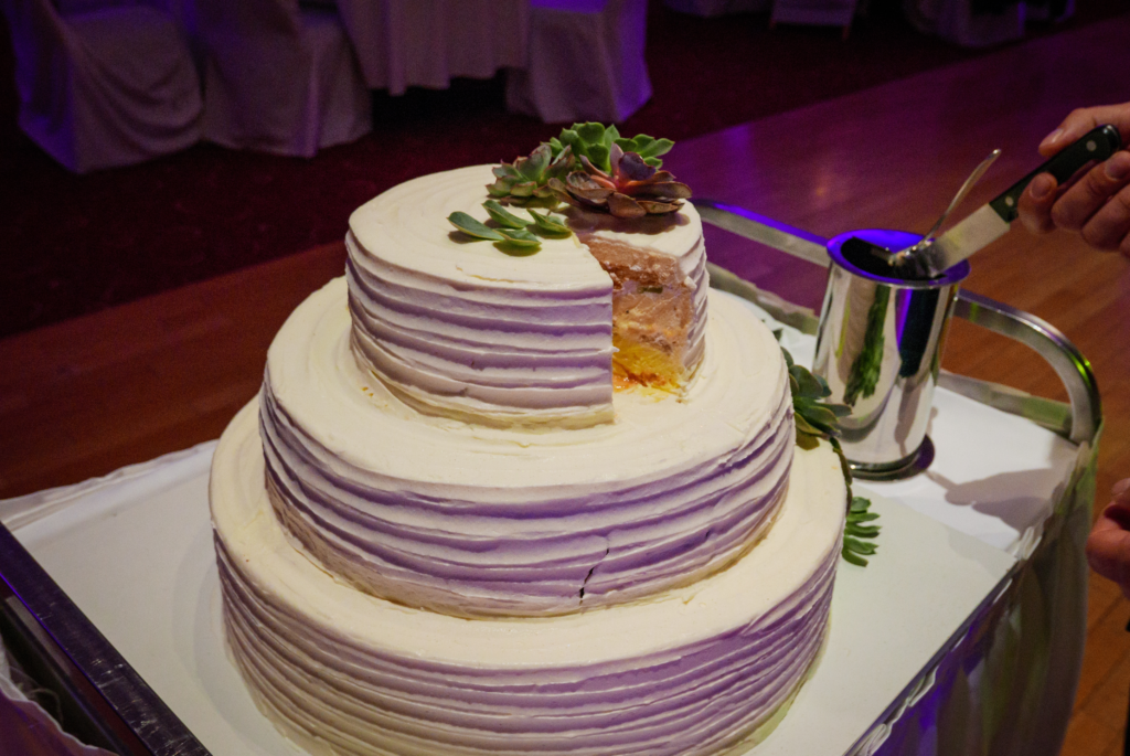 Three-tier wedding cake with a modern design, featuring smooth fondant, gold accents, and elegant floral decorations.