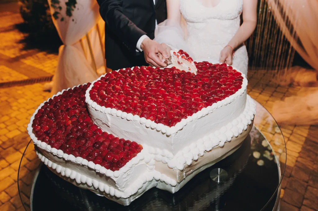 Beautiful wedding scene with a happy couple sharing a kiss, Bride and groom cutting a heart-shaped wedding cake covered with fresh strawberries.