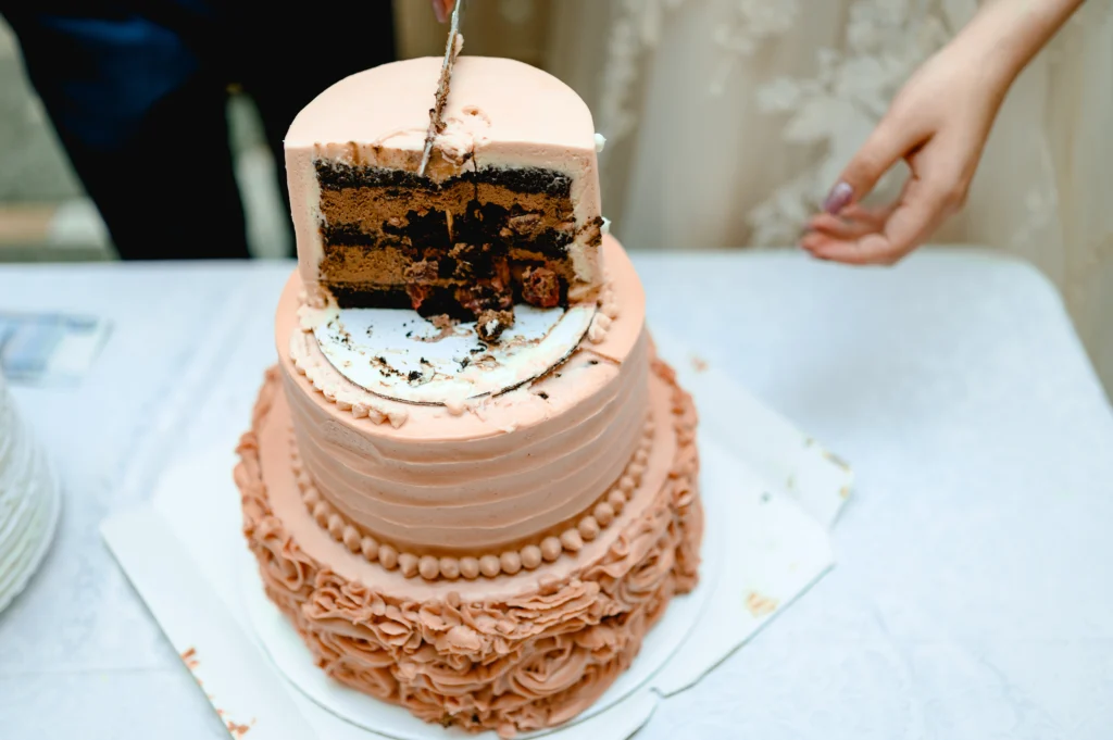 Two-tier wedding cake with pink frosting being cut, revealing chocolate layers inside.