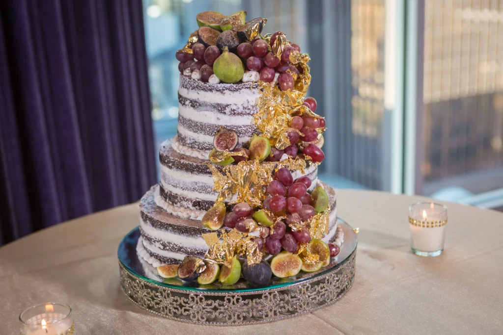 our-tier wedding cake with a rustic design, featuring a semi-naked frosting finish and decorated with fresh flowers and berries.